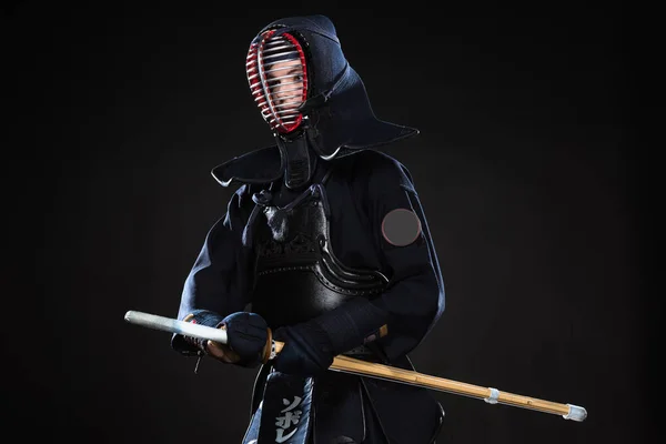 Combatiente Kendo en casco sosteniendo espada de bambú y mirando hacia otro lado en negro - foto de stock