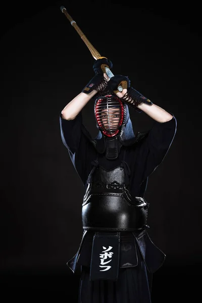 Combatiente Kendo en armadura practicando con espada de bambú sobre negro - foto de stock