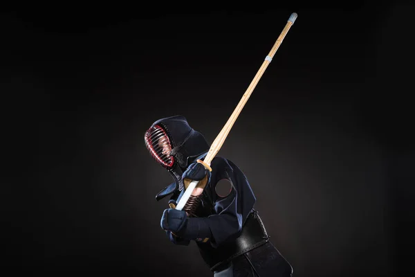 Combatiente Kendo en armadura practicando con espada de bambú sobre negro - foto de stock