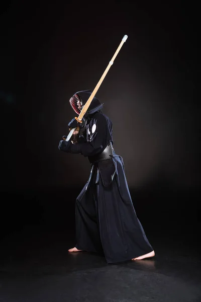 Visão de comprimento total do lutador kendo em armadura praticando com espada de bambu em preto — Fotografia de Stock