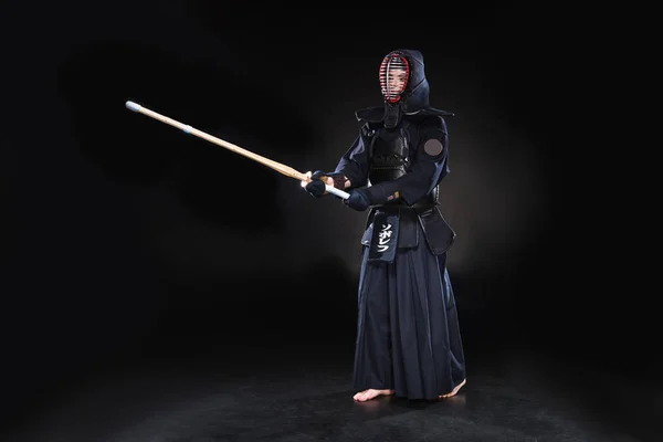 Visão de comprimento total do lutador kendo em armadura praticando com espada de bambu em preto — Fotografia de Stock