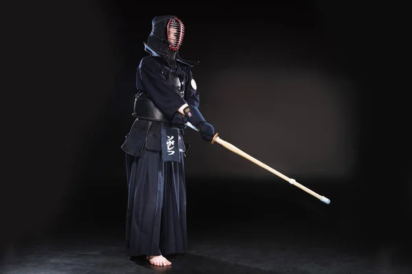 Vista completa del combattente kendo in armatura che si esercita con la spada di bambù sul nero — Foto stock