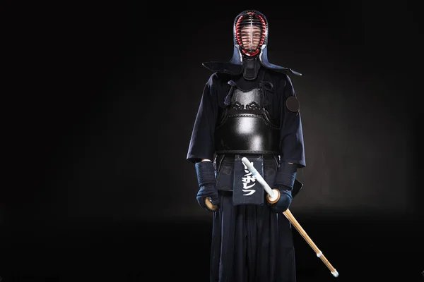 Combatiente Kendo en armadura sosteniendo espada de bambú sobre negro - foto de stock