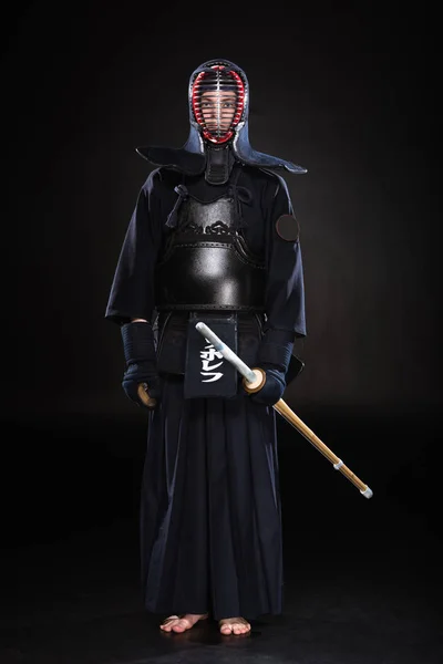 Vue pleine longueur du combattant kendo en armure tenant épée de bambou sur noir — Photo de stock