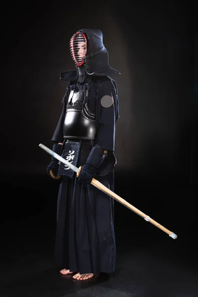 Vista completa de kendo fighter en armadura sosteniendo espada de bambú sobre negro - foto de stock