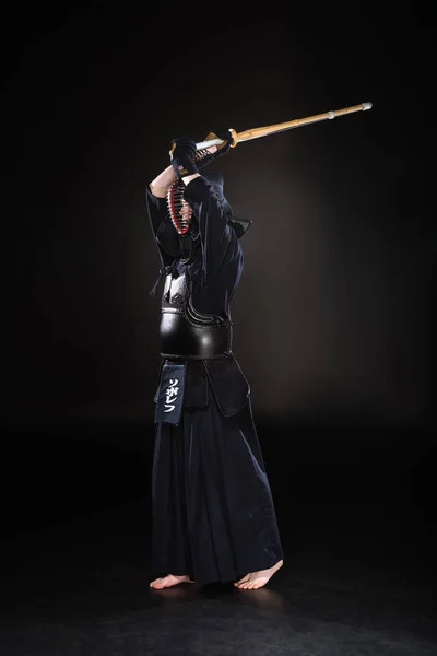 Vista completa de kendo fighter practicando con espada de bambú sobre negro - foto de stock