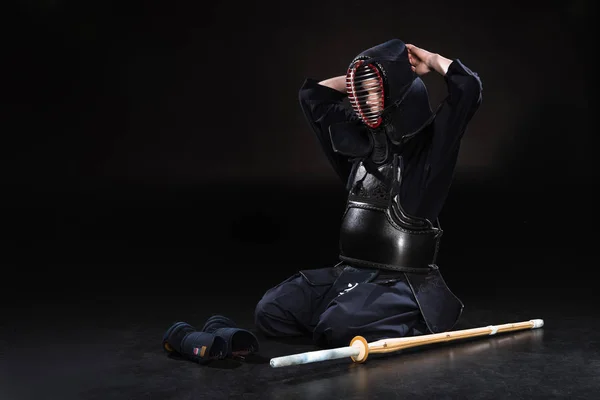 Kendo fighter sitting on floor and taking off helmet on black — Stock Photo