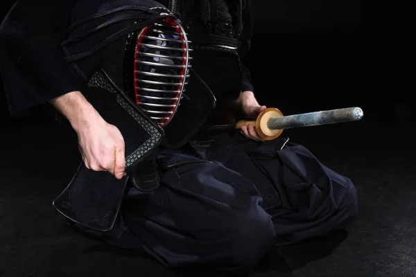 Vista cortada de lutador kendo segurando capacete e espada de bambu em preto — Fotografia de Stock