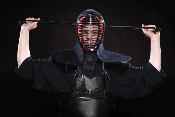 Front view of kendo fighter in armor tying helmet on black — Stock Photo