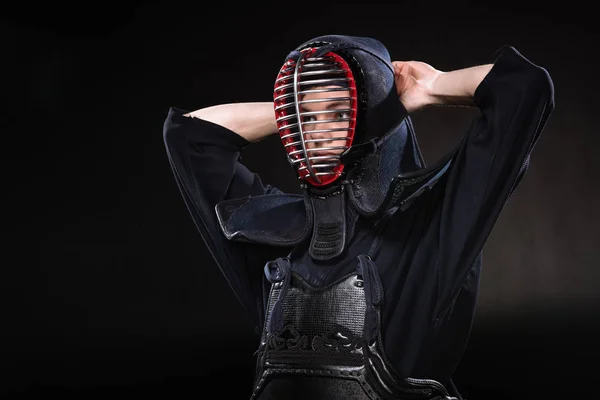 Kendo fighter in armor tying helmet and looking away on black — Stock Photo