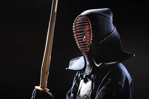 Combatiente Kendo en casco sosteniendo espada de bambú sobre negro - foto de stock