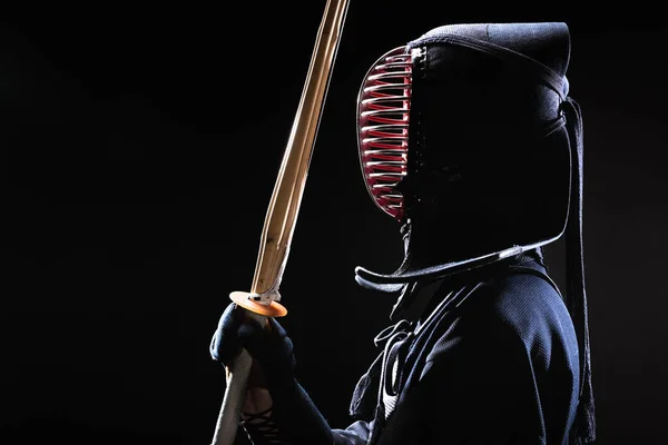 Side view of kendo fighter in traditional helmet holding bamboo sword on black — Stock Photo