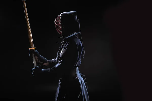 Side view of kendo fighter in traditional helmet holding bamboo sword on black — Stock Photo