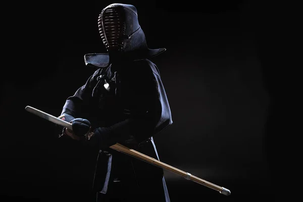 Combatiente Kendo en casco sosteniendo espada de bambú sobre negro - foto de stock