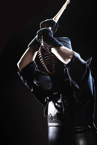 Боец Кендо в доспехах, практикующийся с бамбуковым мечом на черном — стоковое фото