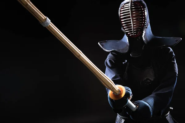 Kendo fighter in helmet holding bamboo sword on black — Stock Photo