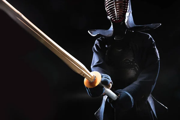 Combatiente Kendo en casco sosteniendo espada de bambú sobre negro - foto de stock