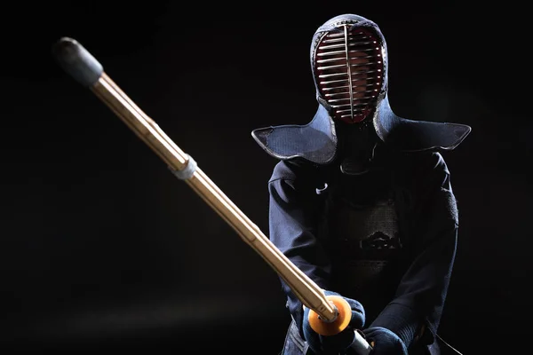 Combatiente Kendo en casco sosteniendo espada de bambú sobre negro - foto de stock