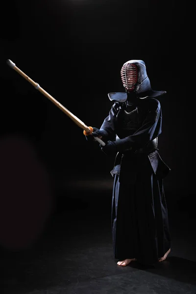 Visão de comprimento total do lutador kendo em armadura praticando com espada de bambu em preto — Fotografia de Stock