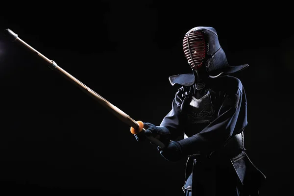 Kendo fighter in armor practicing with bamboo sword isolated on black — Stock Photo