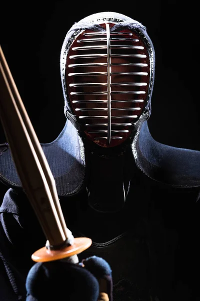 Combatiente Kendo en casco sosteniendo espada de bambú aislado en negro - foto de stock