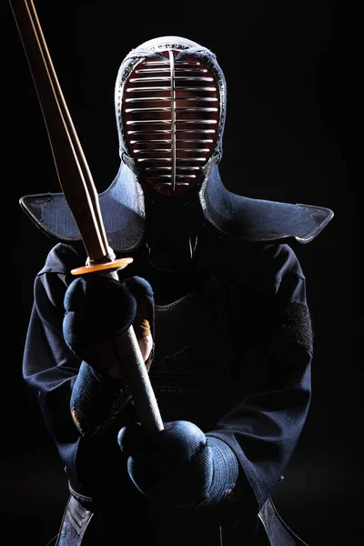 Combatiente Kendo en casco sosteniendo espada de bambú sobre negro - foto de stock