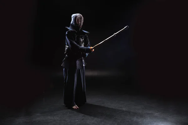 Full length view of kendo fighter in armor practicing with bamboo sword on black — Stock Photo