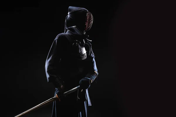 Kendo fighter in helmet holding bamboo sword on black — Stock Photo