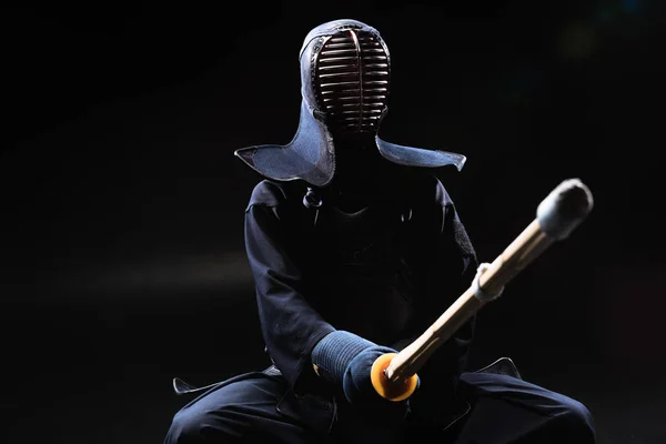 Combatiente Kendo en casco sosteniendo espada de bambú sobre negro - foto de stock