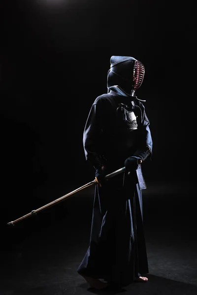 Pleine longueur vue du combattant kendo dans le casque tenant épée de bambou sur noir — Photo de stock