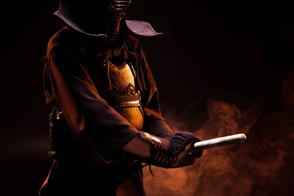 Vista parcial del luchador kendo en armadura sosteniendo espada sobre negro - foto de stock
