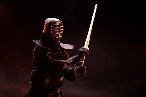 Combatiente Kendo en armadura practicando con espada de bambú sobre negro - foto de stock