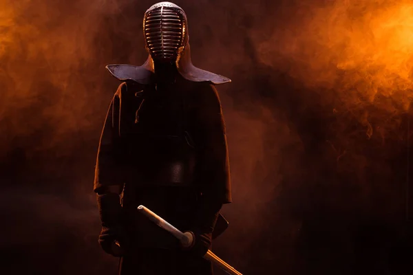 Combatiente Kendo en armadura sosteniendo espada de bambú en humo - foto de stock