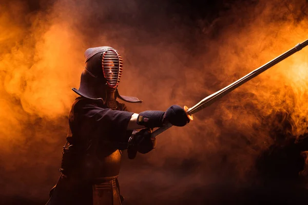 Combatiente Kendo en armadura practicando con espada de bambú en humo - foto de stock