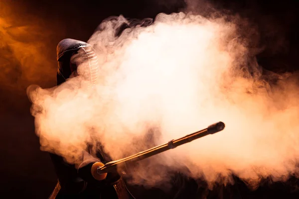 Combatiente Kendo en casco sosteniendo espada de bambú en humo - foto de stock