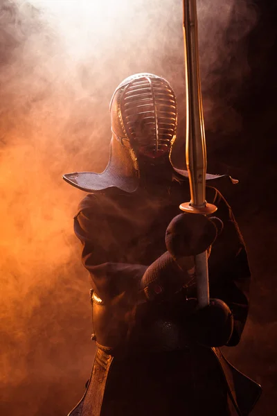 Combatiente Kendo en armadura sosteniendo espada de bambú en humo - foto de stock