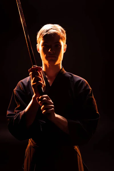 Junger Mann im Kimono hält Kendo-Schwert auf schwarz — Stockfoto