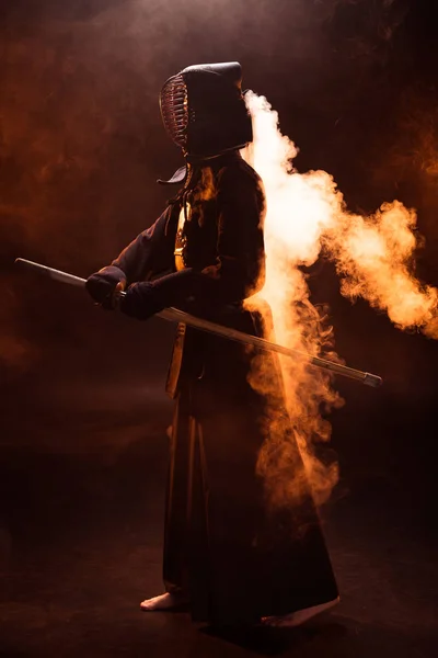 Vista completa de kendo fighter en armadura sosteniendo espada de bambú en humo - foto de stock