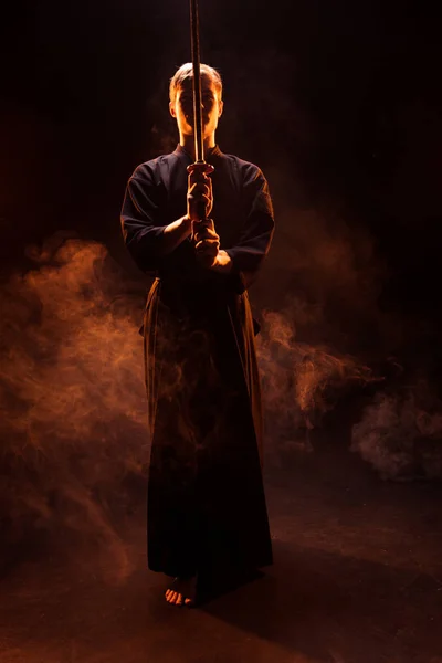 Полный обзор молодого человека в кимоно, держащего меч Кендо в дыму — стоковое фото