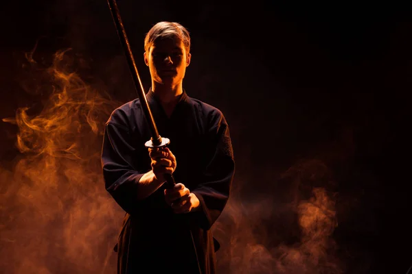 Young man in kimono holding kendo sword in smoke — Stock Photo