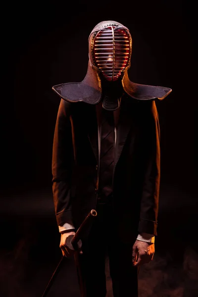 Mann im Anzug und Kendo-Helm mit Bambusschwert auf schwarz — Stockfoto