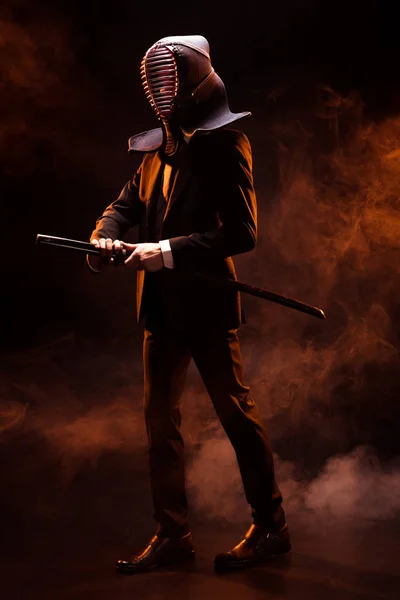 Вид на повну довжину боєць Кендо в офіційному одязі і шоломі, що тримає бамбуковий меч на темряві — стокове фото
