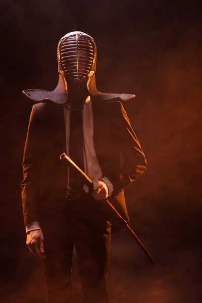 Kendo lutador em desgaste formal e capacete segurando espada de bambu no escuro — Fotografia de Stock