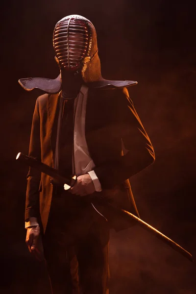 Mann in offizieller Kleidung und Kendo-Helm mit Bambusschwert auf dunklem Hintergrund — Stockfoto