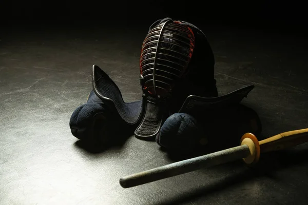 Luvas Kendo, capacete e espada de bambu na superfície escura — Fotografia de Stock