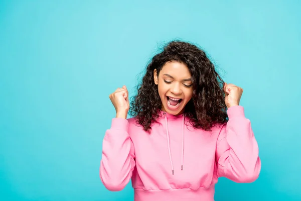 Excited curly african american girl smiling while celebrating triumph isolated on blue — Stock Photo