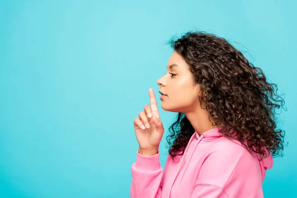 Side view of curly african american girl showing hush sign isolated on blue — Stock Photo