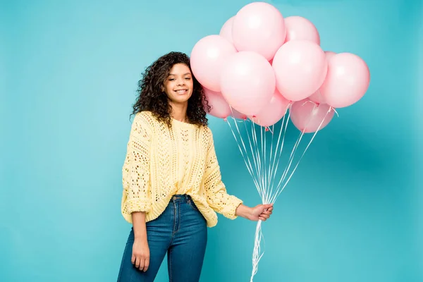 Happy curly african american girl holding pink air balloons on blue — Stock Photo