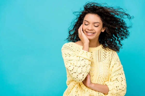 Pretty curly african american woman touching face while smiling isolated on blue — Stock Photo