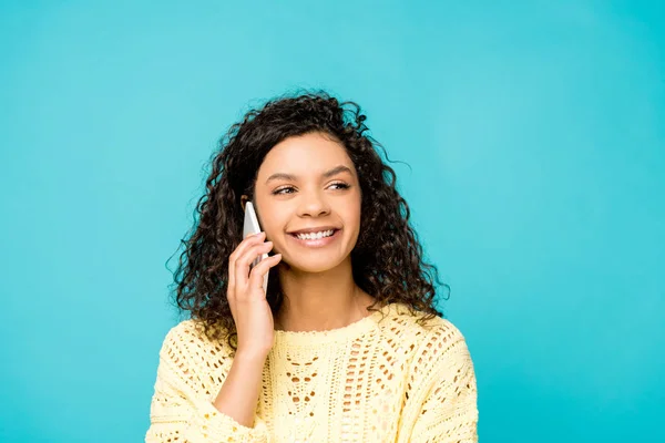 Pretty curly african american woman smiling while talking on smartphone isolated on blue — Stock Photo